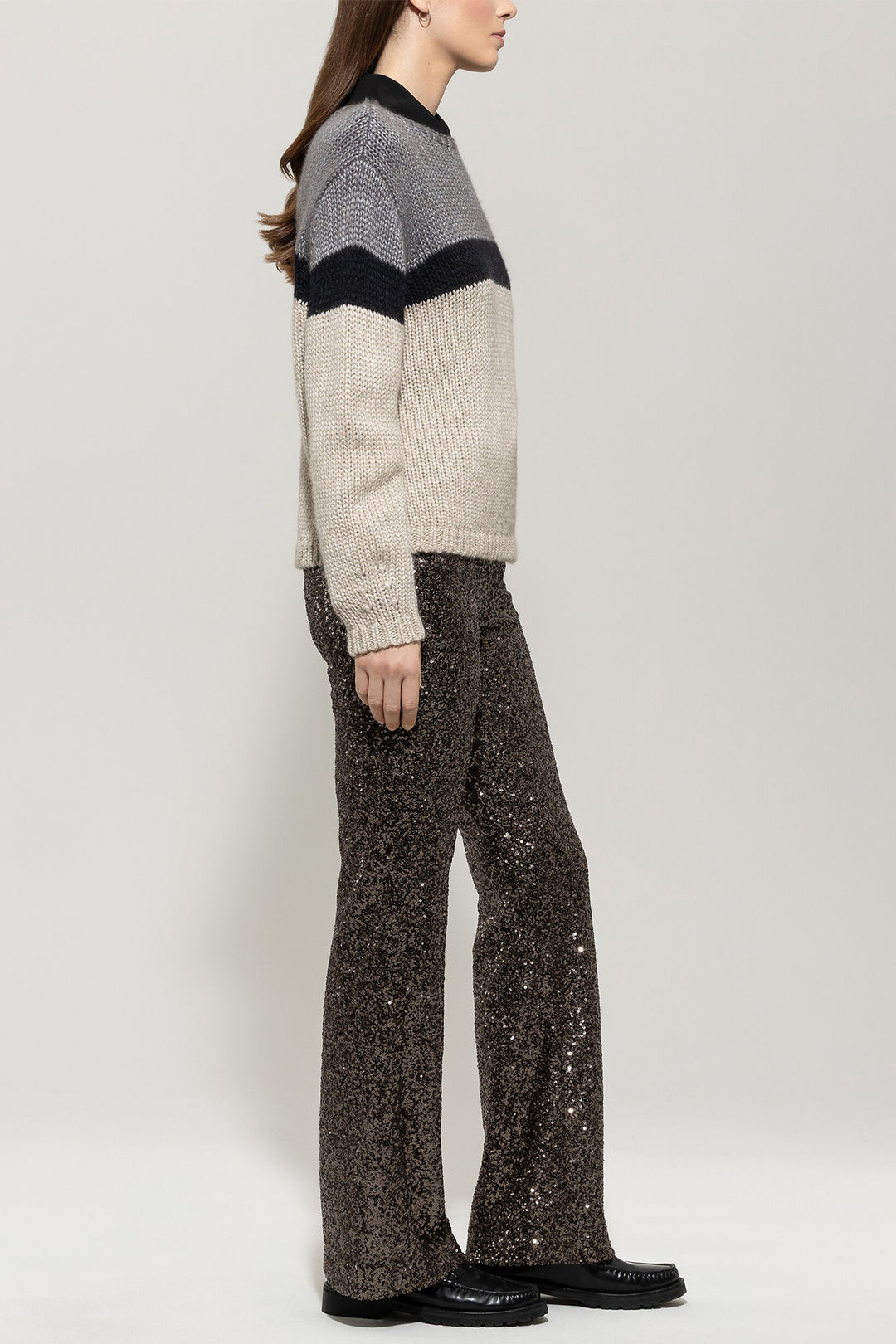 Person wearing a striped sweater and sequin pants on a plain background