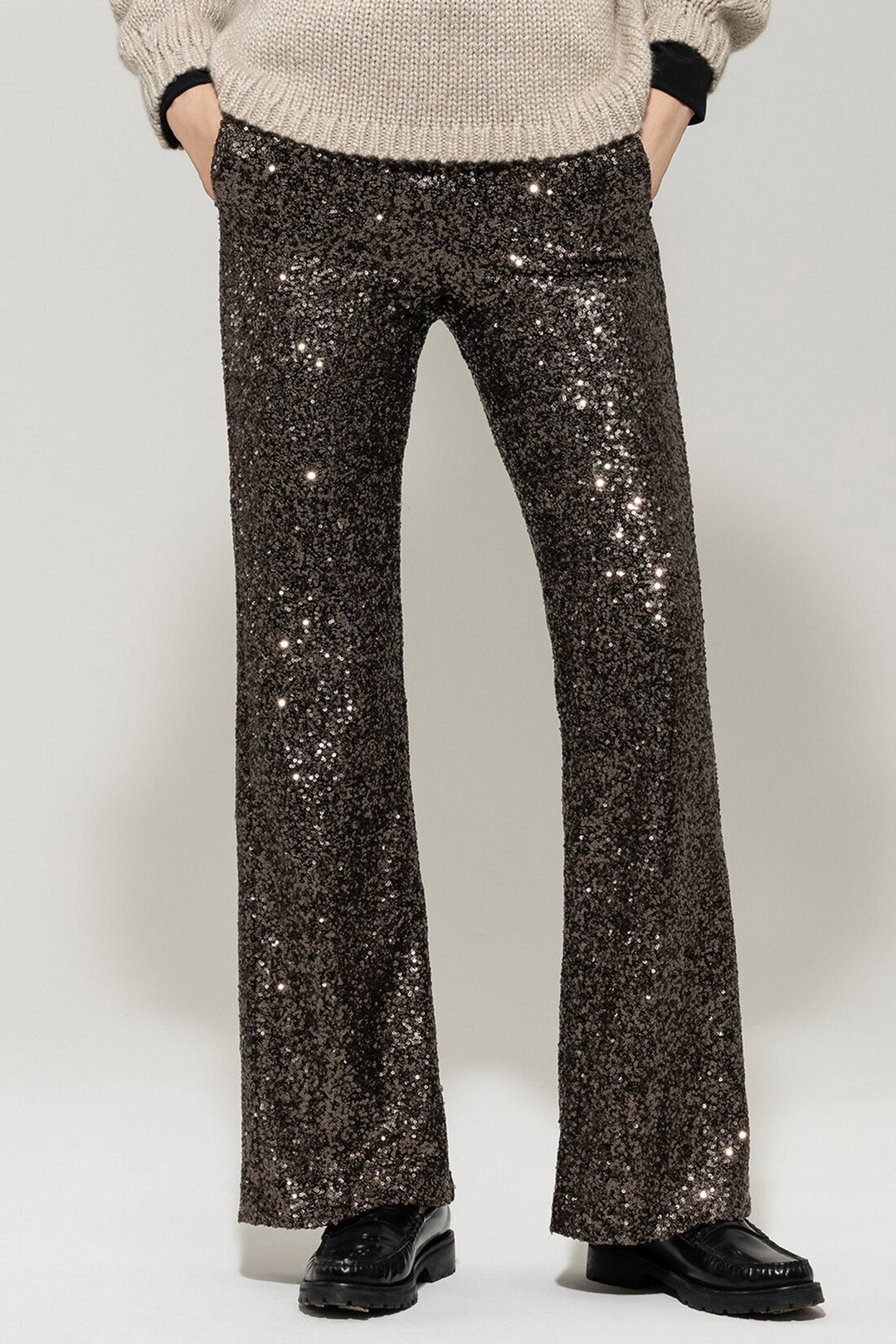 Person wearing sparkly black pants and a beige sweater on a white background