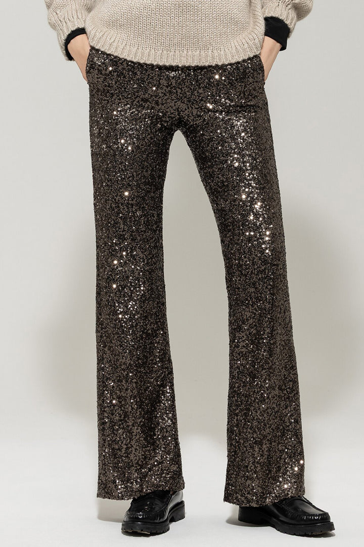 Person wearing sparkly black pants and a beige sweater on a white background