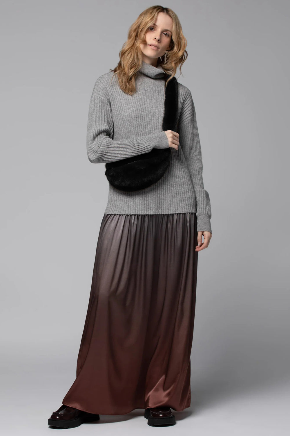 Woman wearing a gray sweater and brown skirt against a gray background