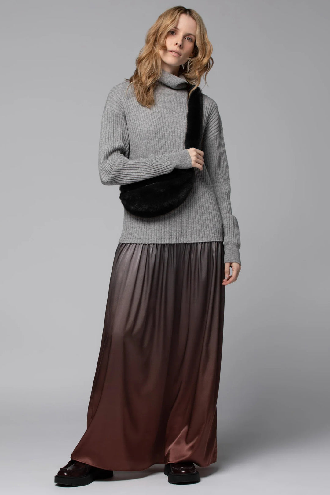 Woman wearing a gray sweater and brown skirt against a gray background
