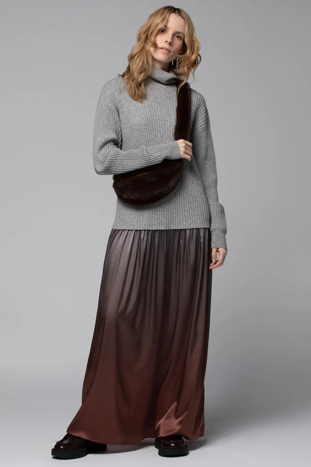 Woman wearing a gray sweater and brown skirt against a plain background