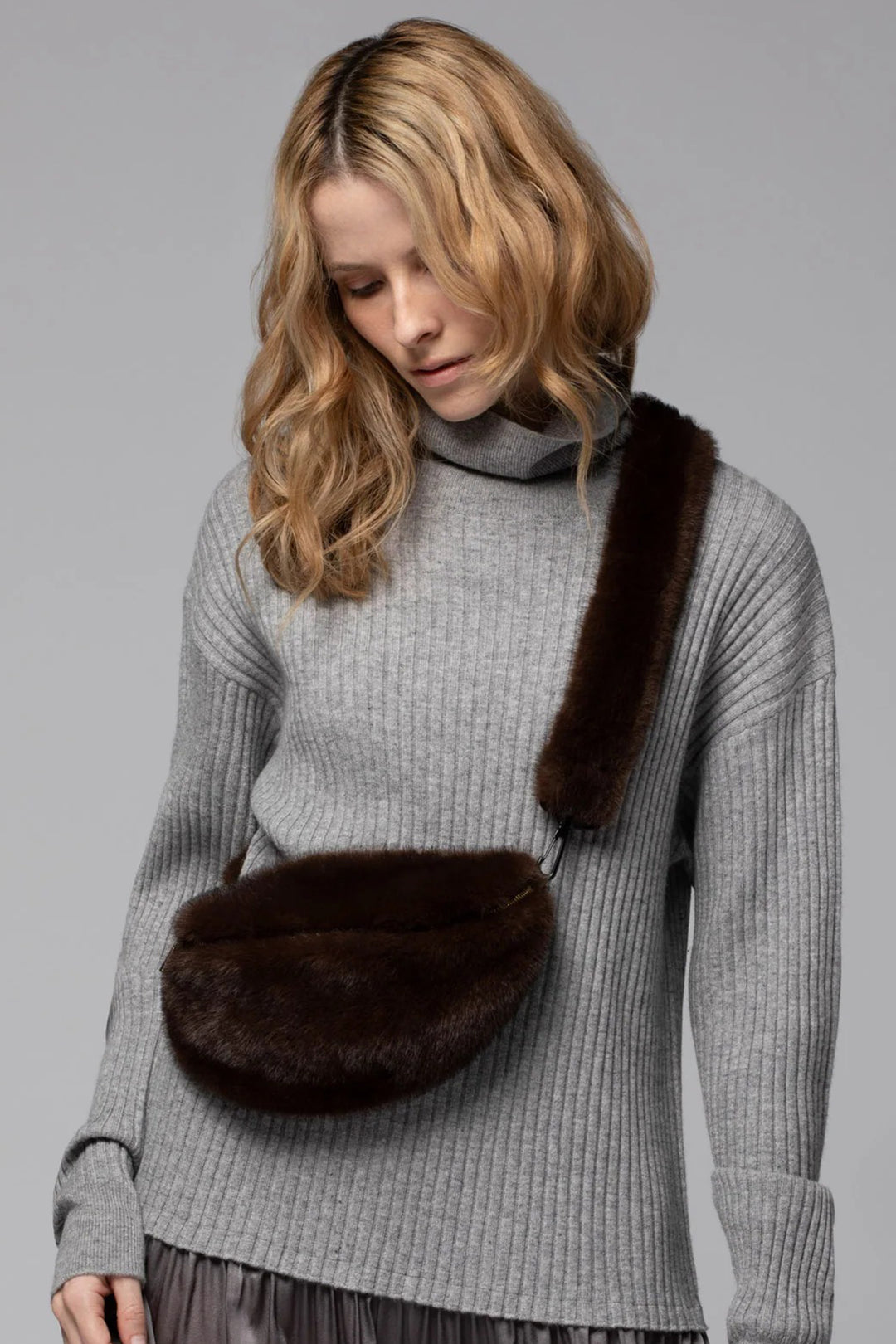 Woman wearing a gray sweater with a brown fur bag on a gray background