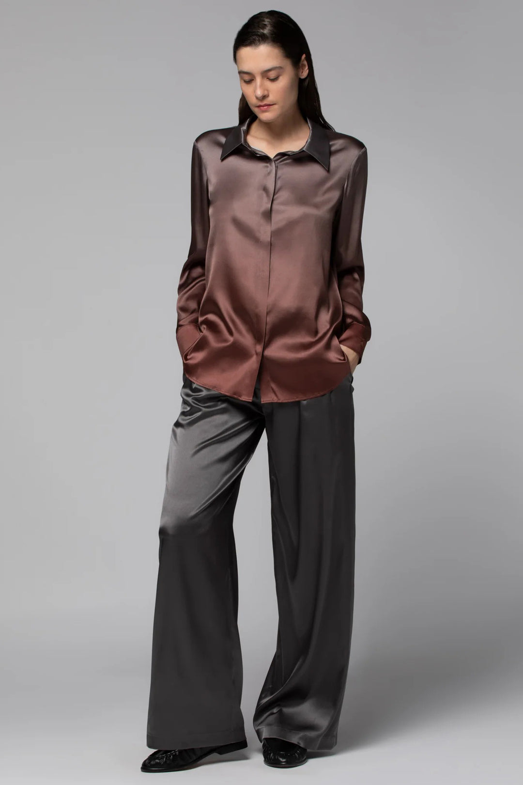 Woman wearing a brown satin blouse and gray pants on a plain background