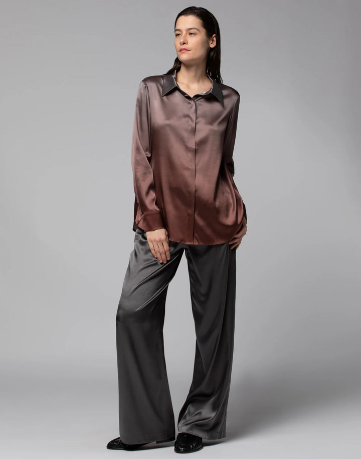 Woman wearing a brown satin shirt and gray pants on a gray background