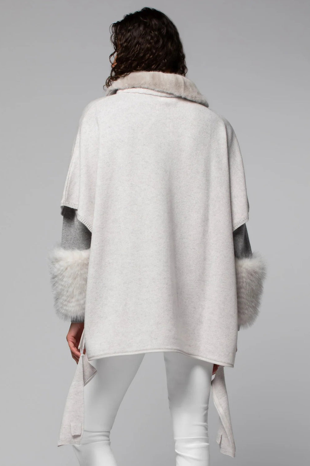 Person wearing a light gray poncho with fur trim on a plain background