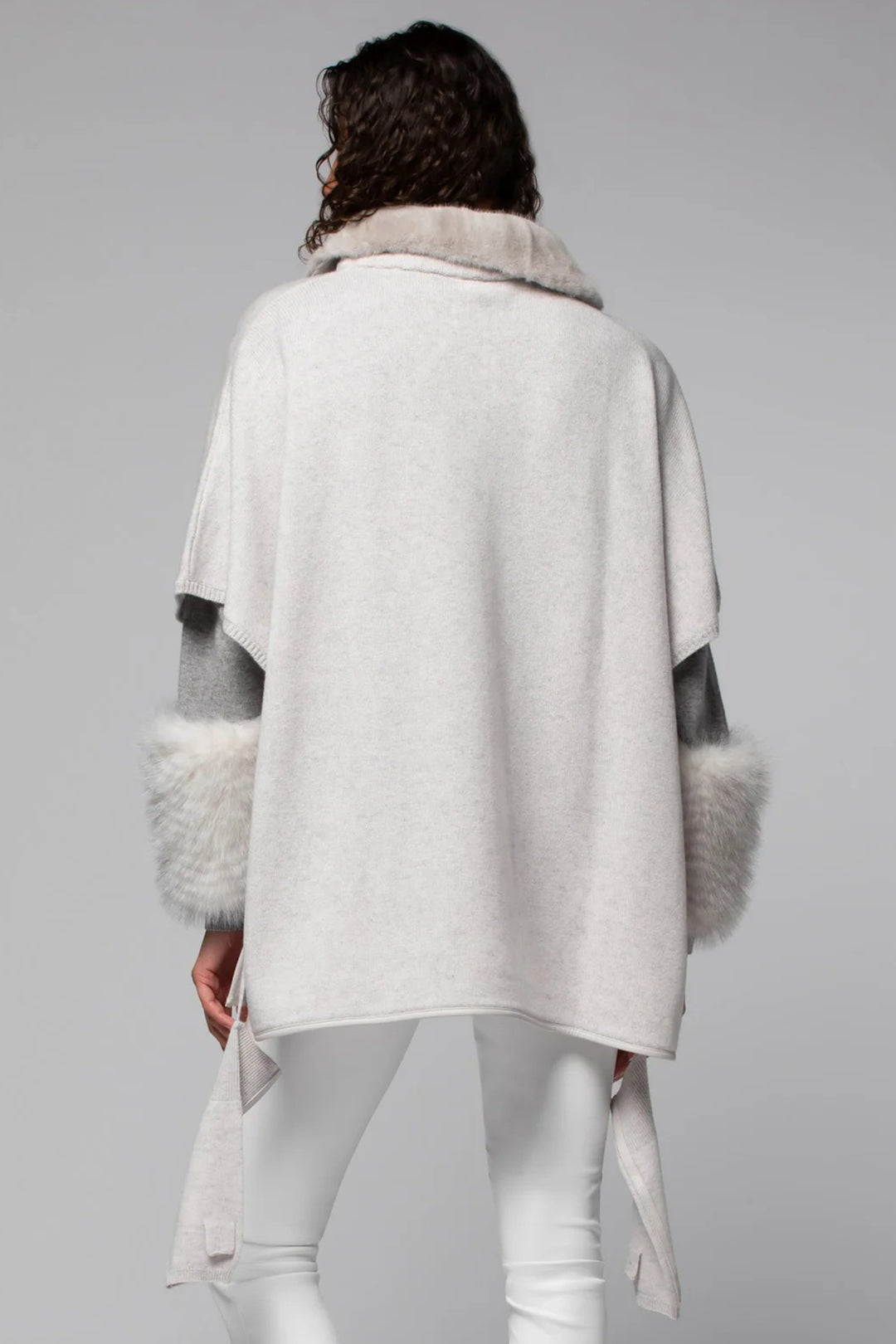 Person wearing a light gray poncho with fur trim on a plain background