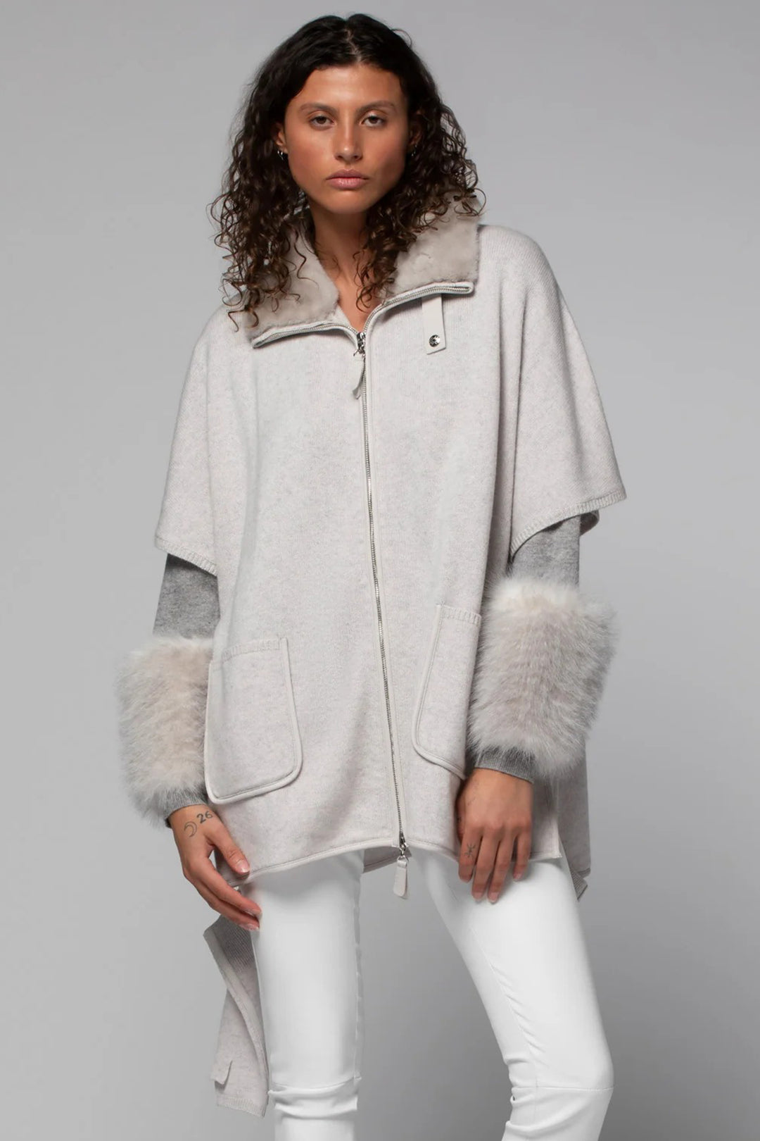 Woman wearing a light gray poncho with fur trim on a gray background