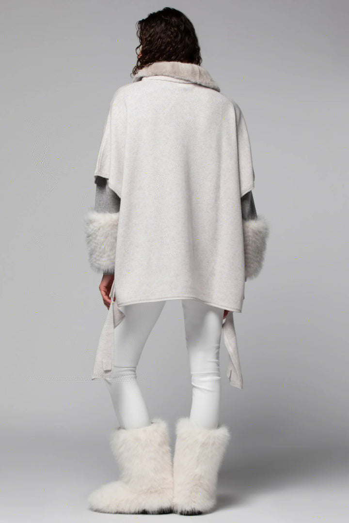 Person wearing a white poncho with fur trim and matching white boots on a gray background