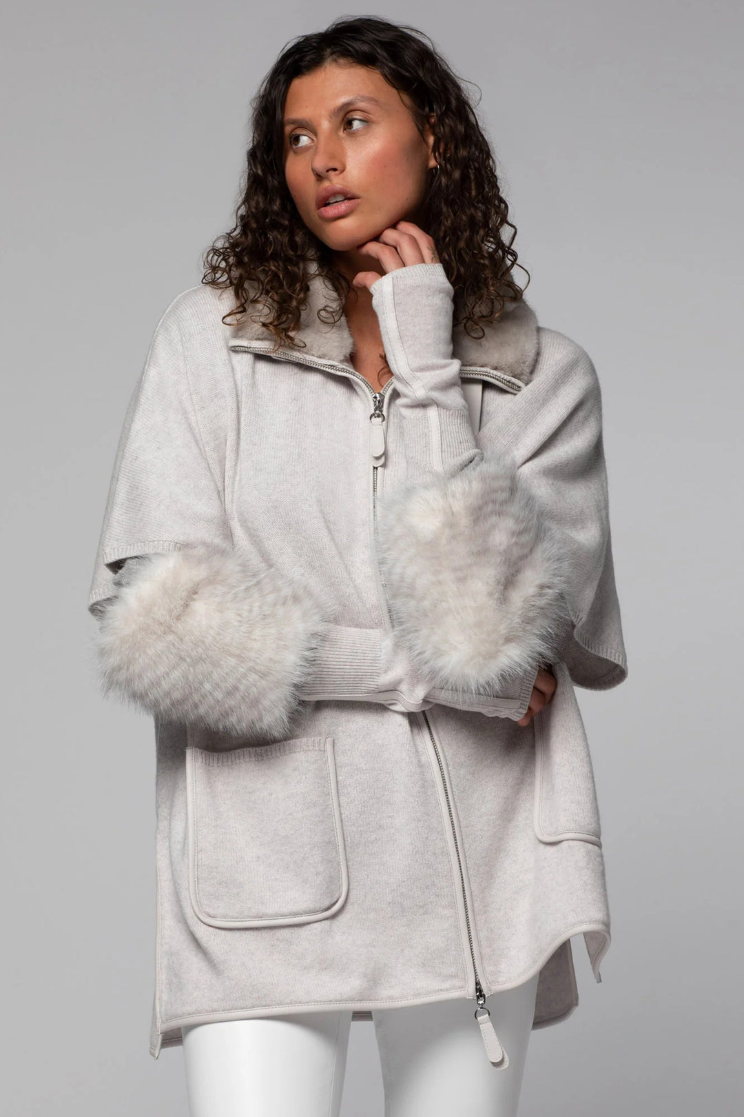 Woman wearing a light gray coat with fur trim on a plain background