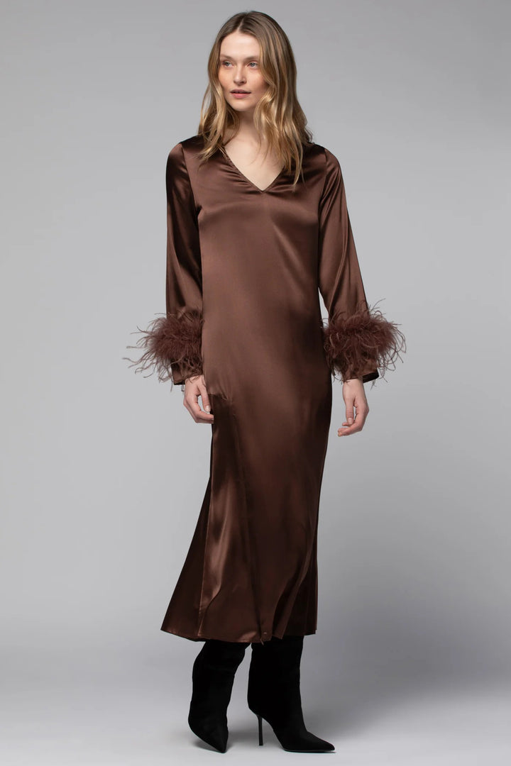 Woman wearing a brown satin dress with feathered cuffs on a gray background