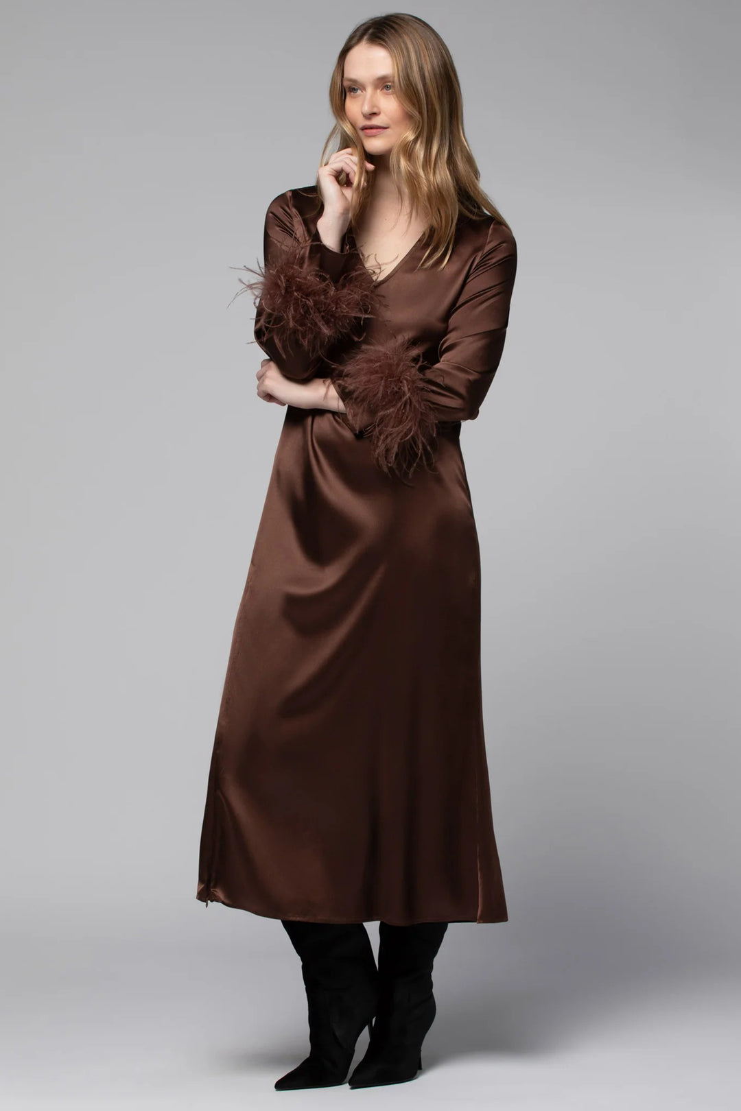 Woman wearing a brown satin dress with feathered sleeves on a gray background