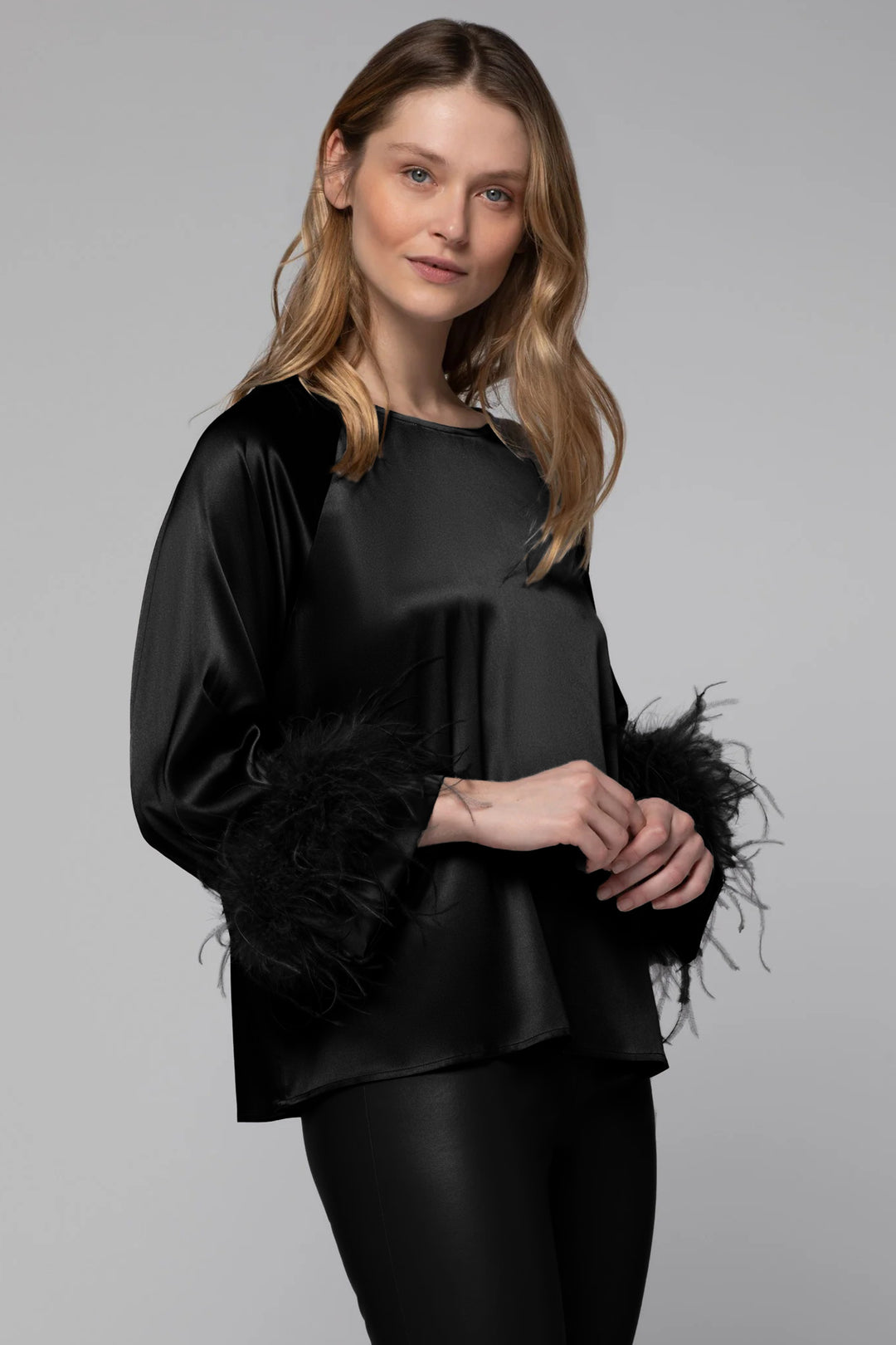 Woman wearing a black silk top with feathered sleeves against a gray background