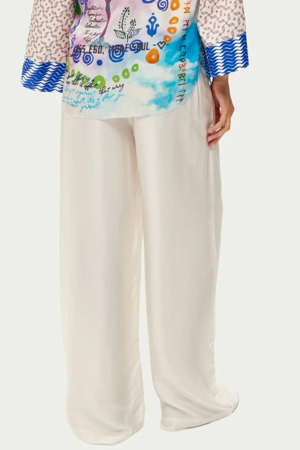 Colorful top with abstract patterns and white pants on a white background