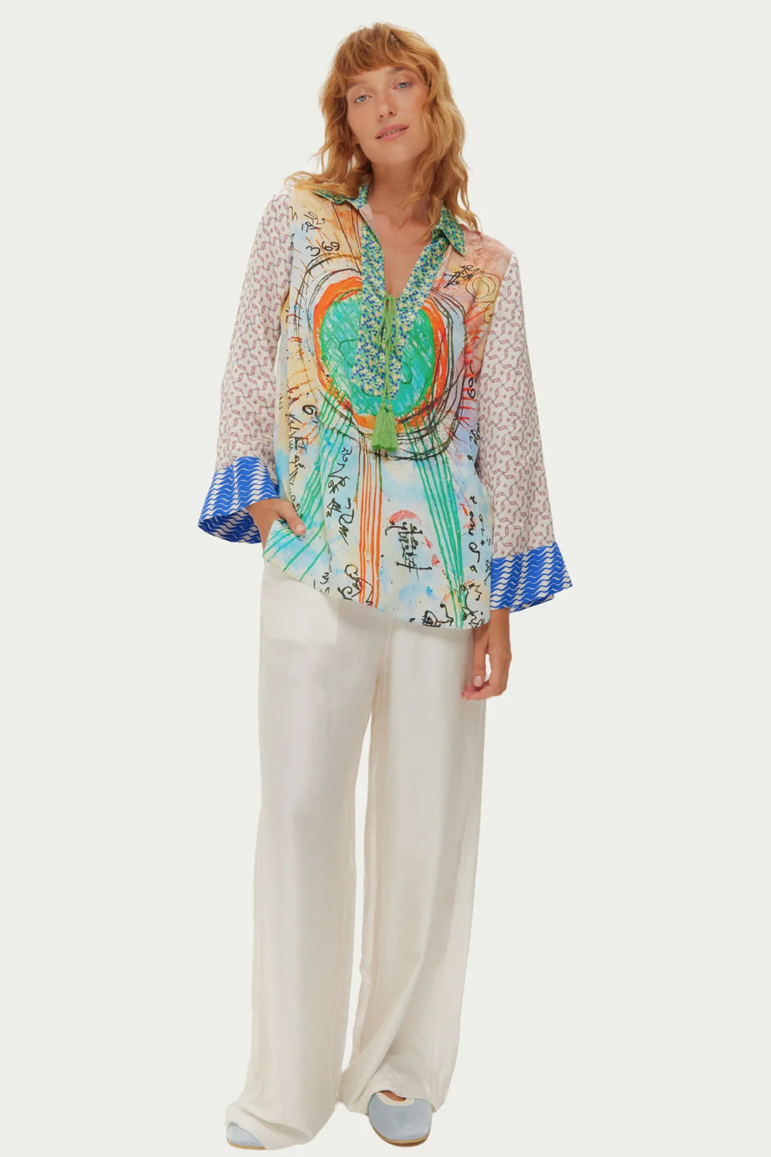 Woman wearing a colorful patterned blouse with wide-leg pants on a white background