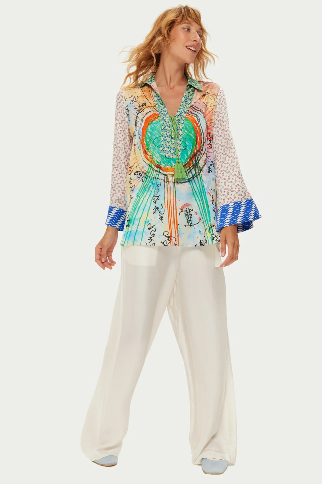 Woman wearing a colorful patterned blouse and white pants on a white background