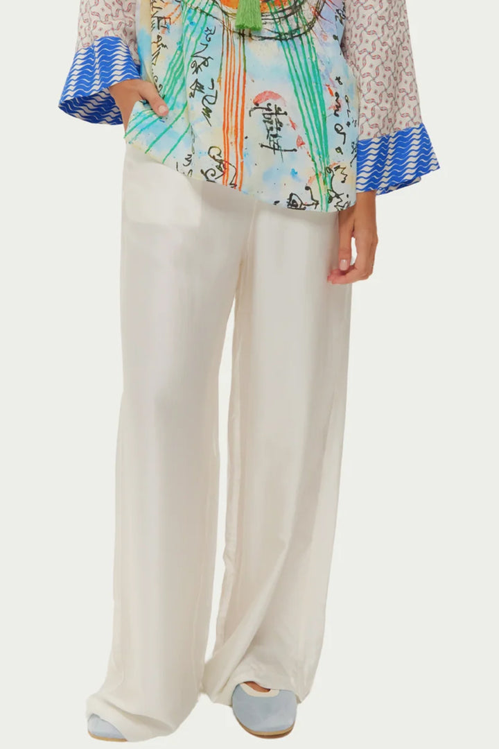 Person wearing a colorful top with blue and white patterns and white pants on a light gray background
