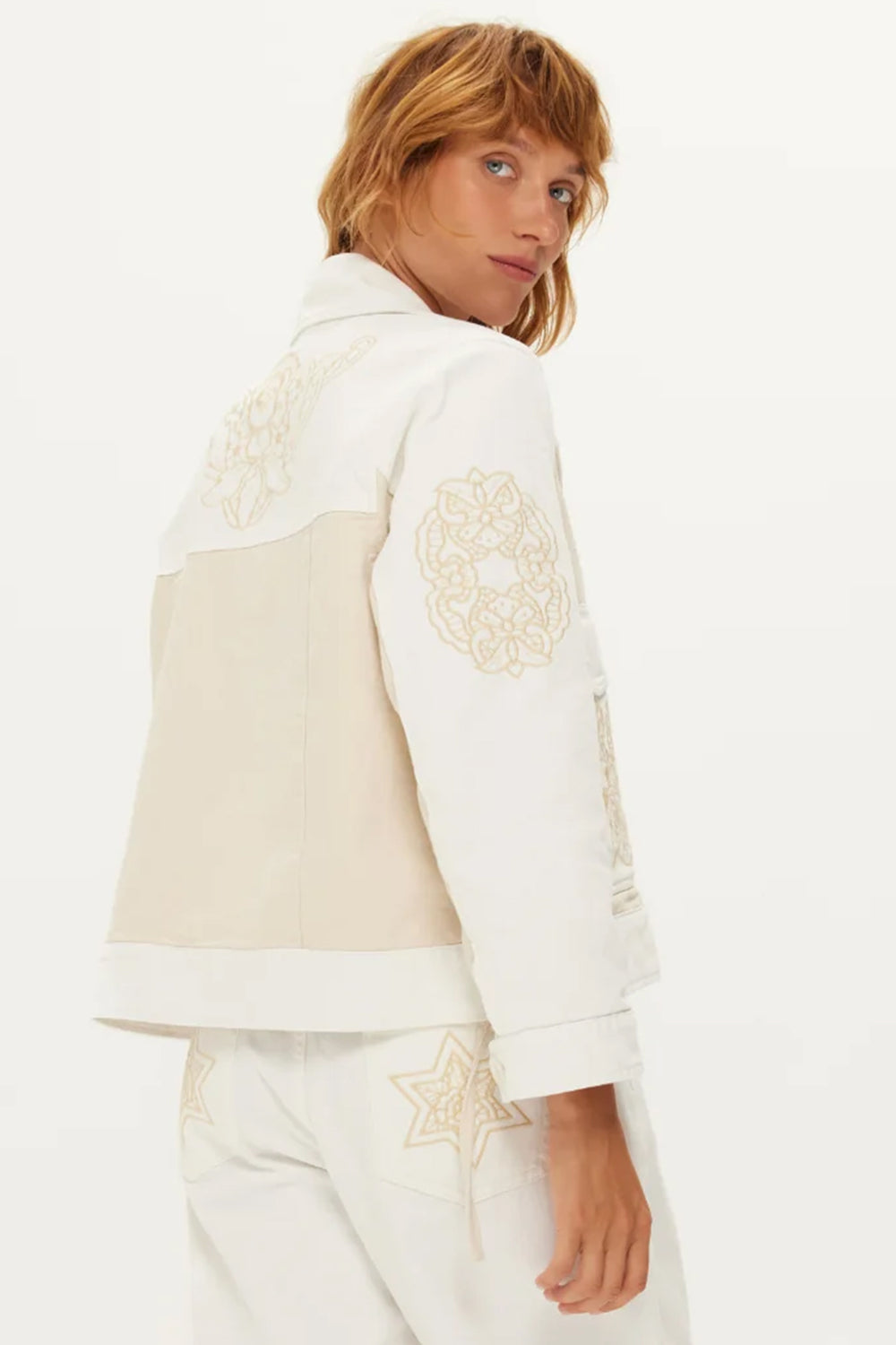 Person wearing a white and beige jacket with floral embroidery on a white background