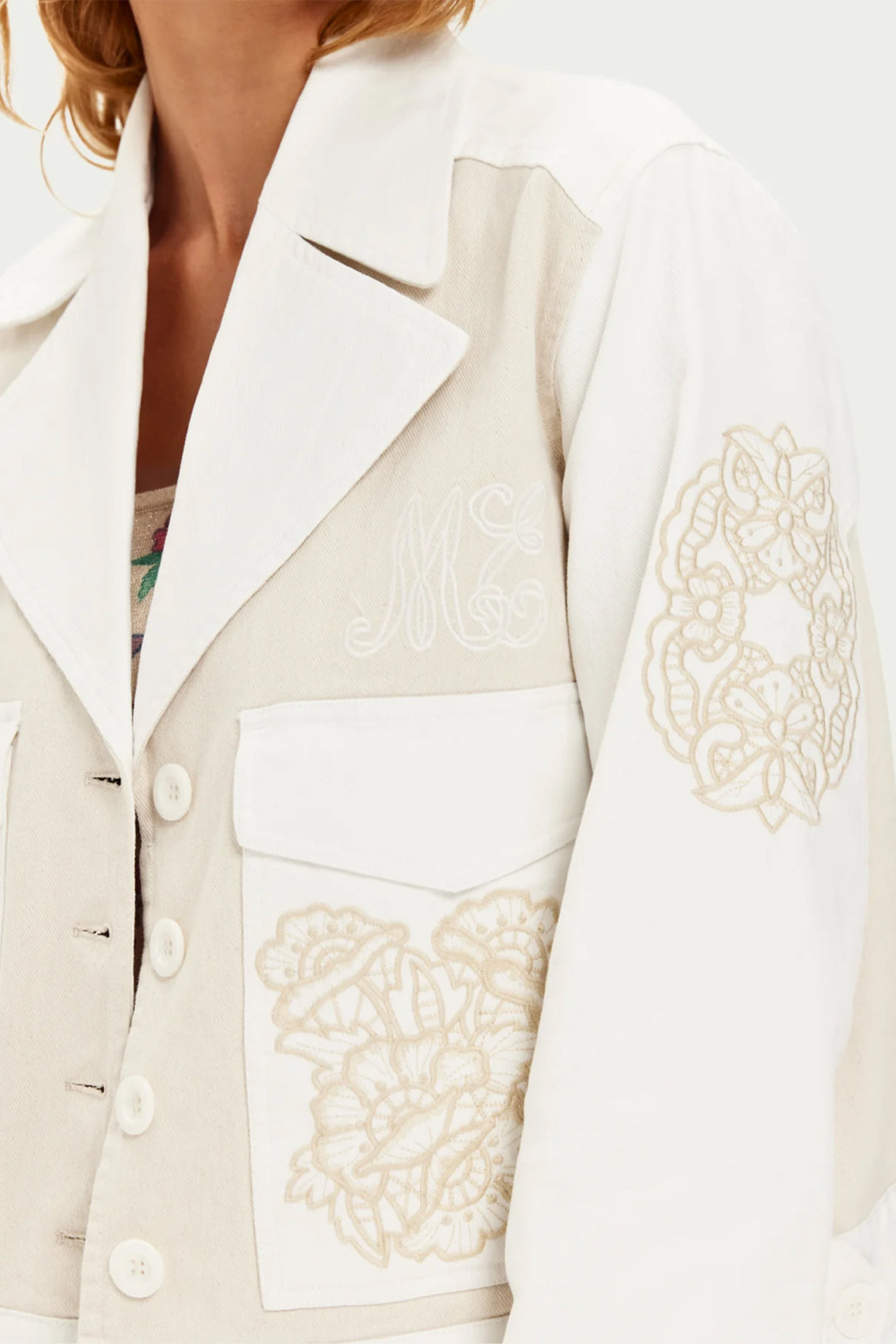 Close-up of a beige blazer with intricate lace detailing on a white background