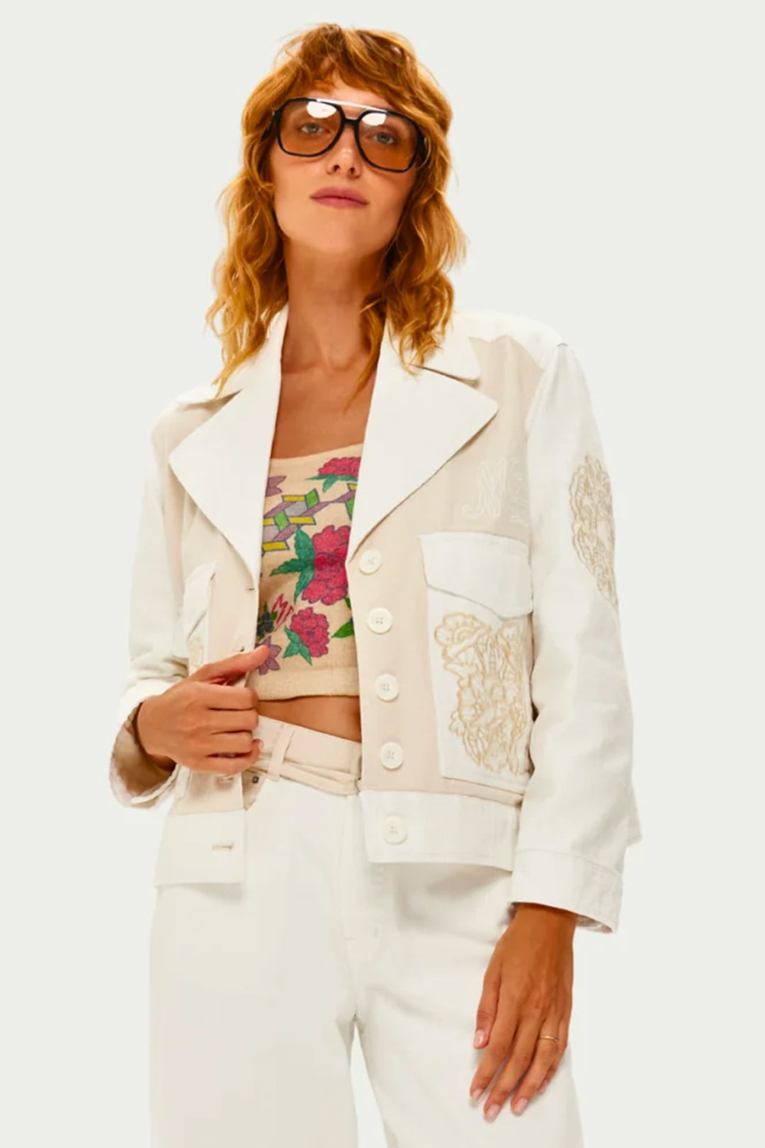 Woman wearing a white jacket with floral top and white pants on a light background