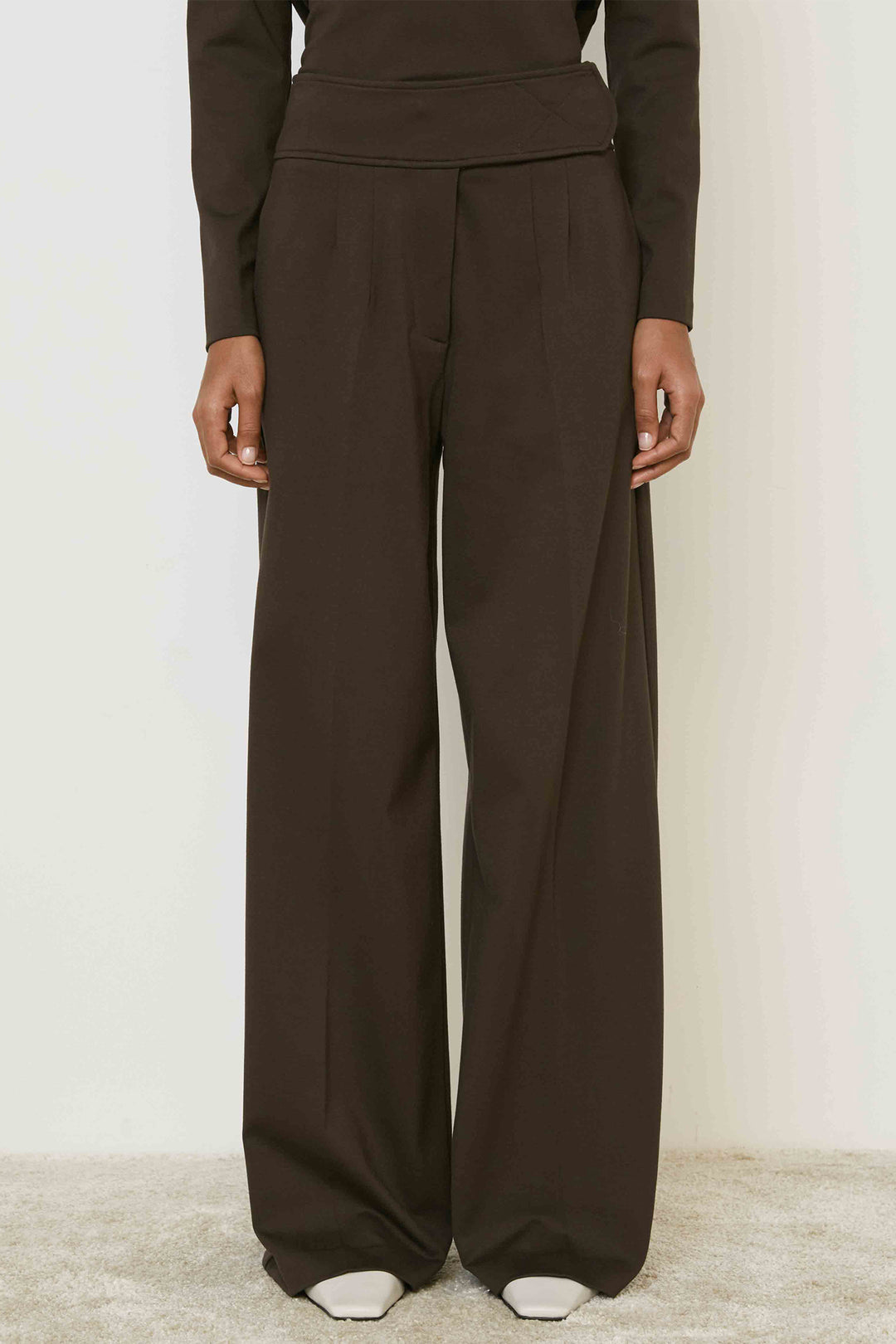 Person wearing brown long-sleeve top and wide-leg pants on a plain background