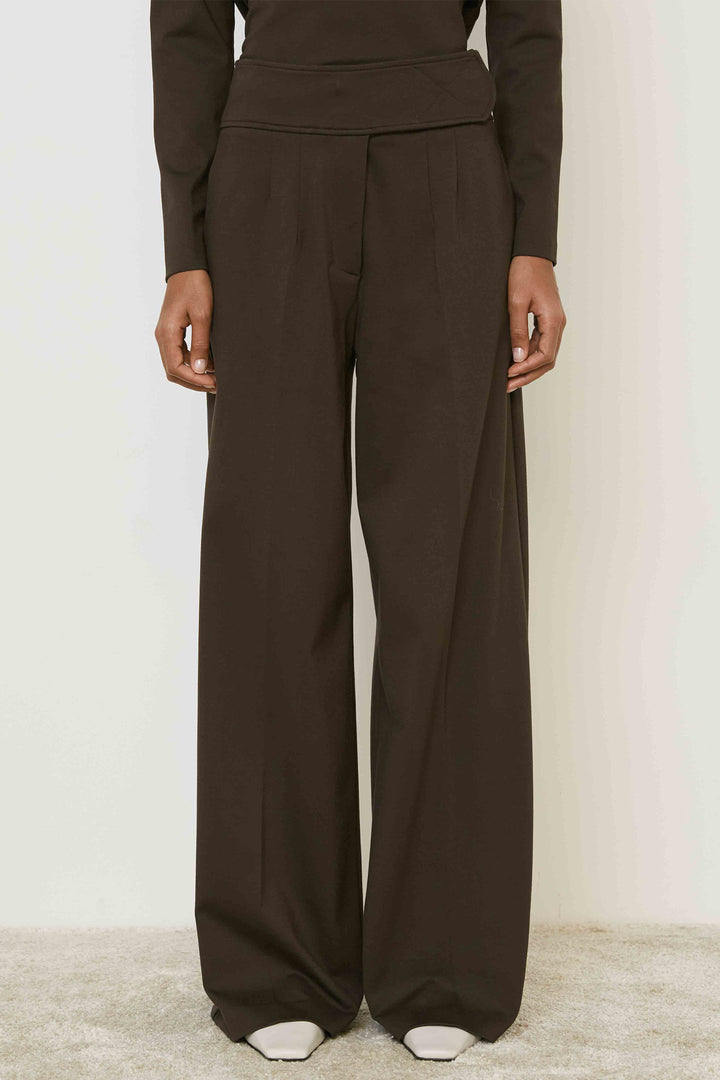 Person wearing brown long-sleeve top and wide-leg pants on a plain background