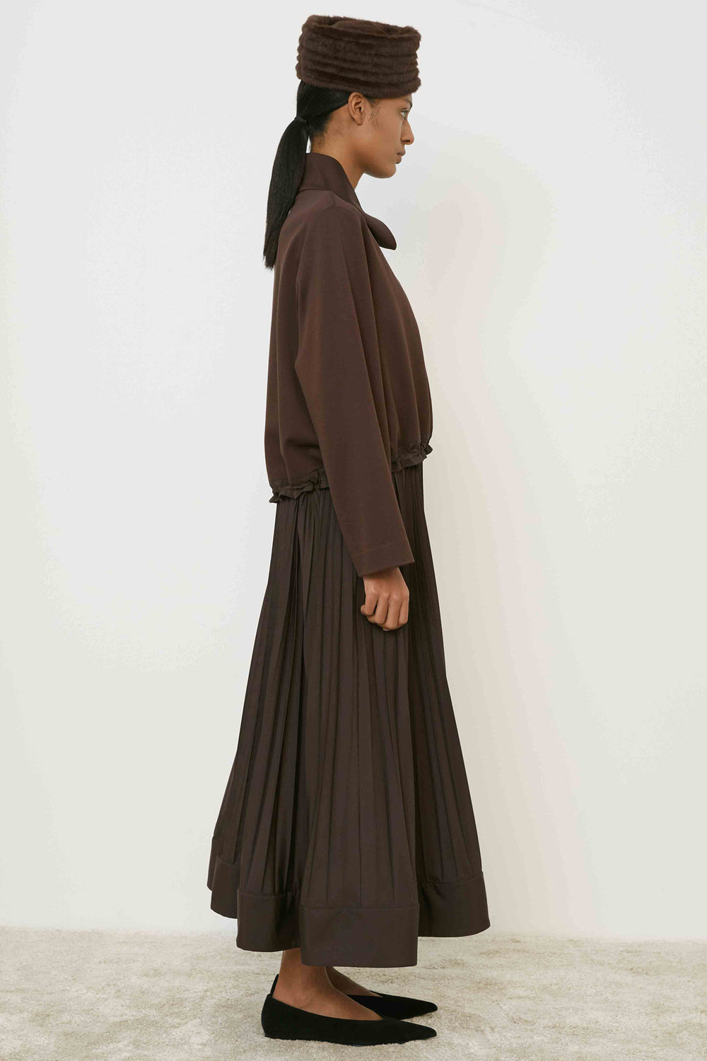 Woman wearing a brown outfit with a matching hat against a white background