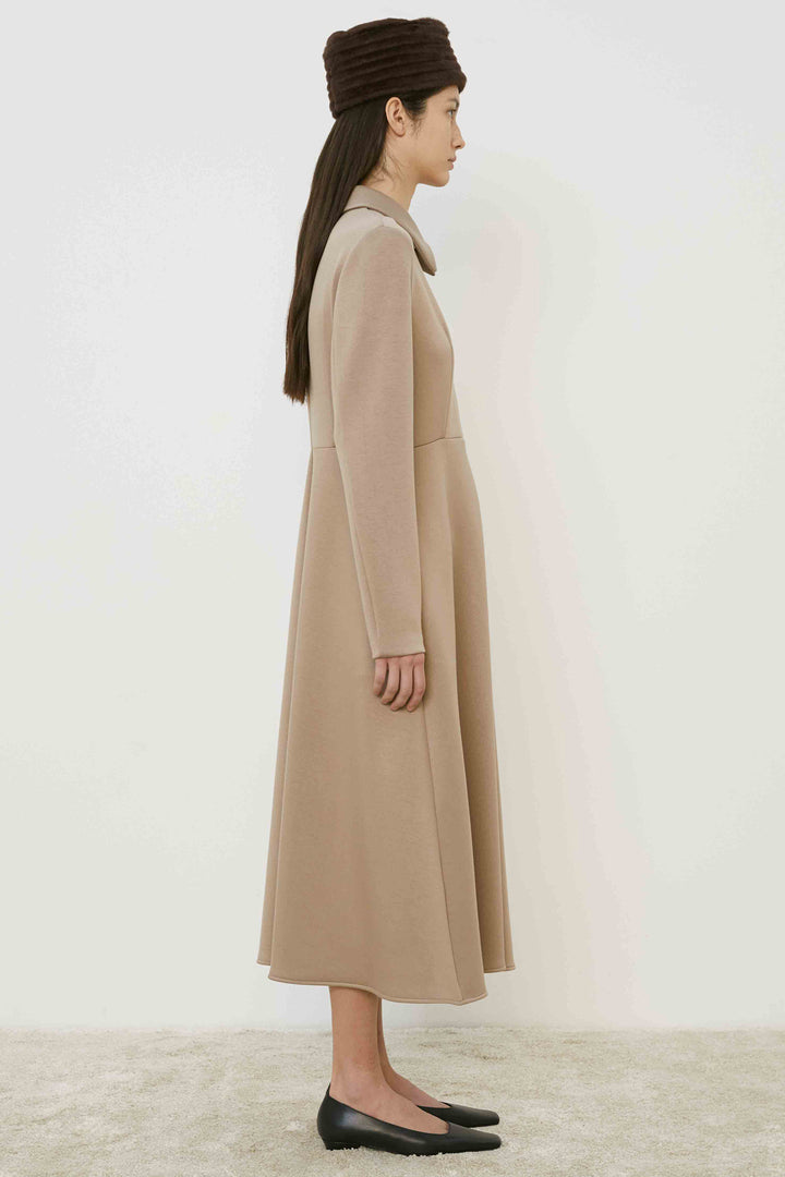 Woman wearing a long beige coat dress and black shoes on a white background