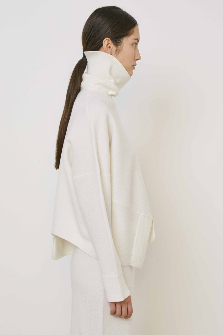 Woman wearing a white turtleneck and skirt against a plain background
