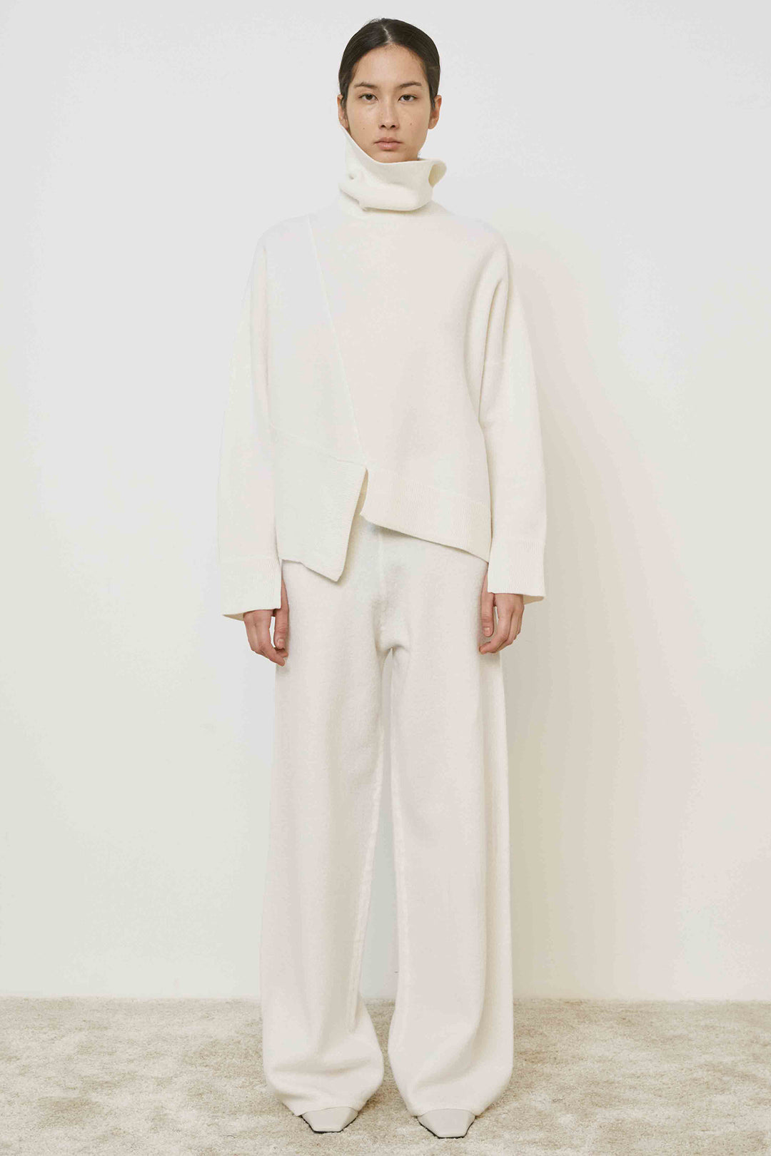 Person wearing a white outfit with a high collar against a plain background