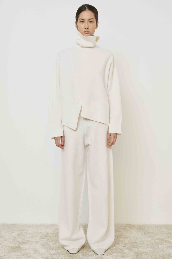 Person wearing a white outfit with a high collar against a plain background