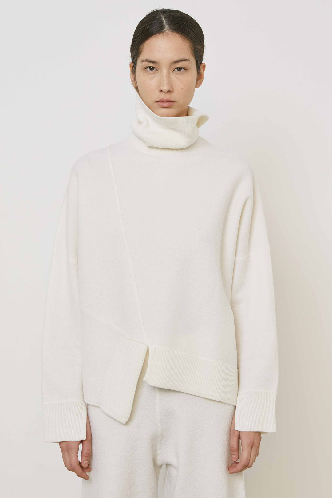 Person wearing a white turtleneck sweater and pants on a plain background