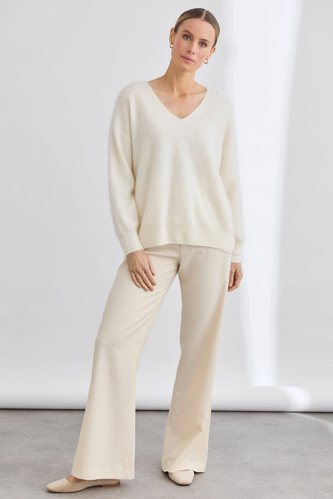 Woman wearing a cream-colored sweater and pants against a white background