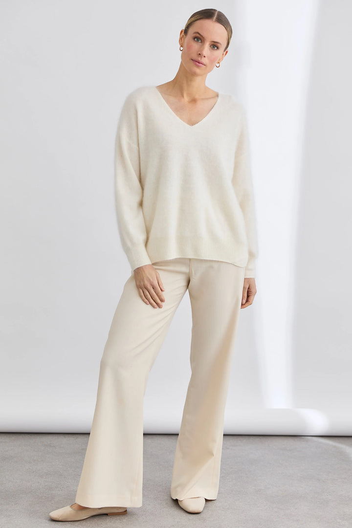 Woman wearing a cream-colored sweater and pants against a white background