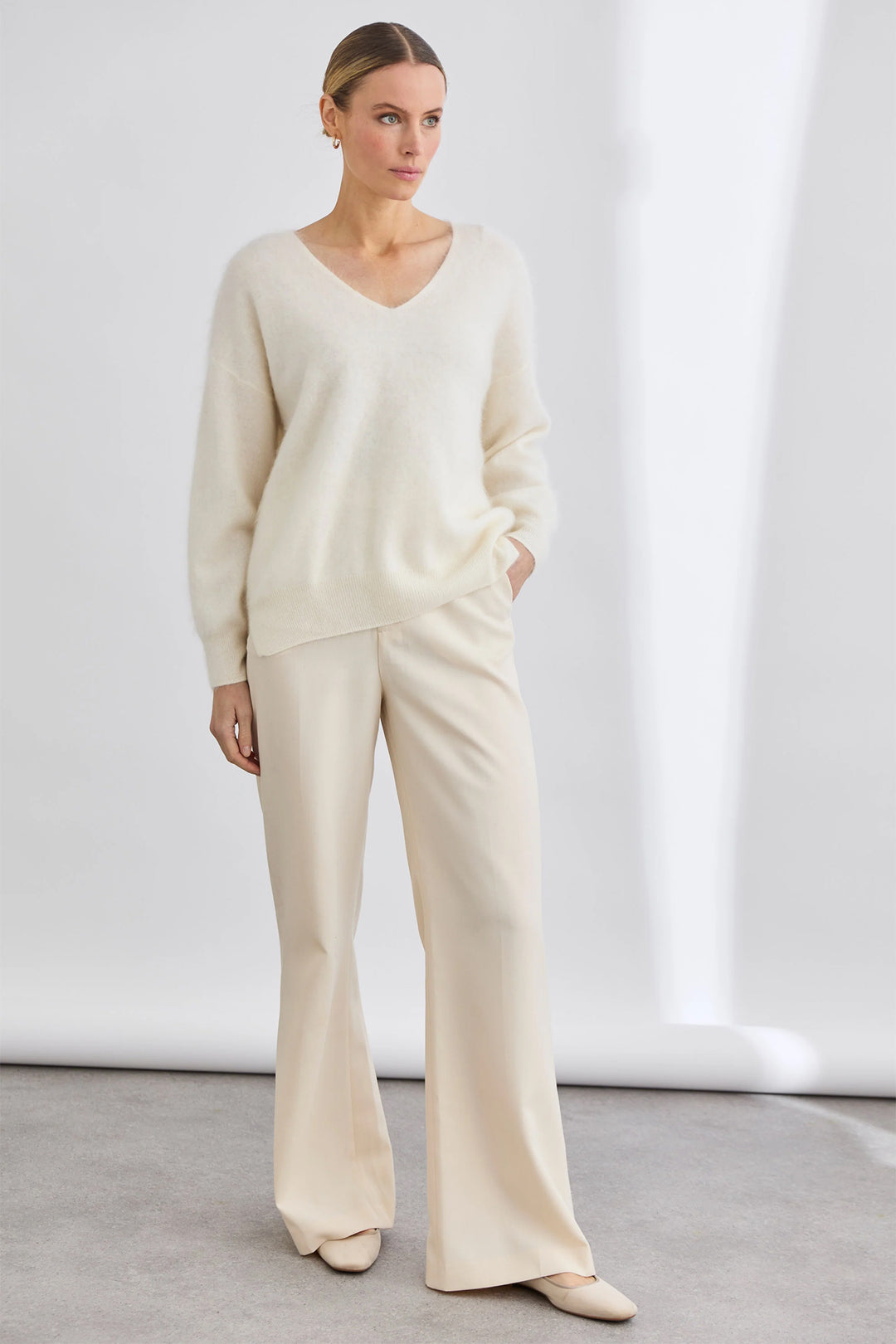 Woman wearing a cream-colored outfit with a sweater and pants on a white background
