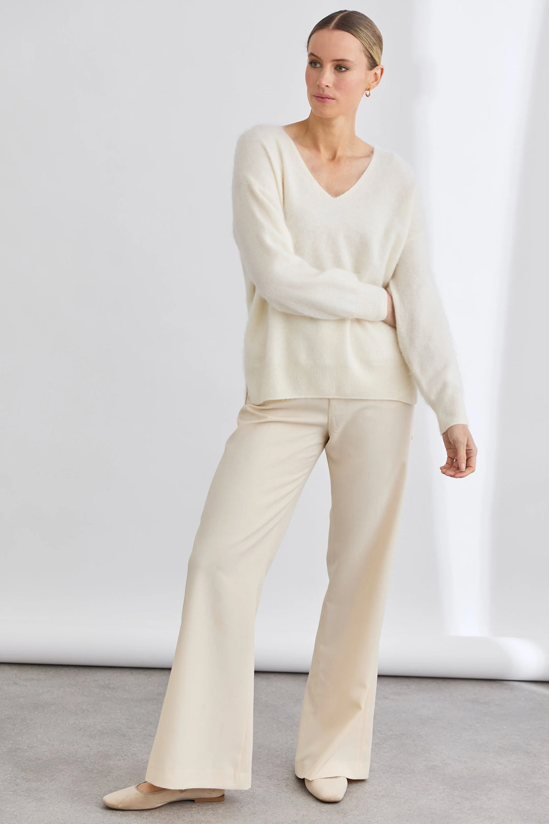 Woman wearing a cream-colored outfit with a sweater and pants against a white background