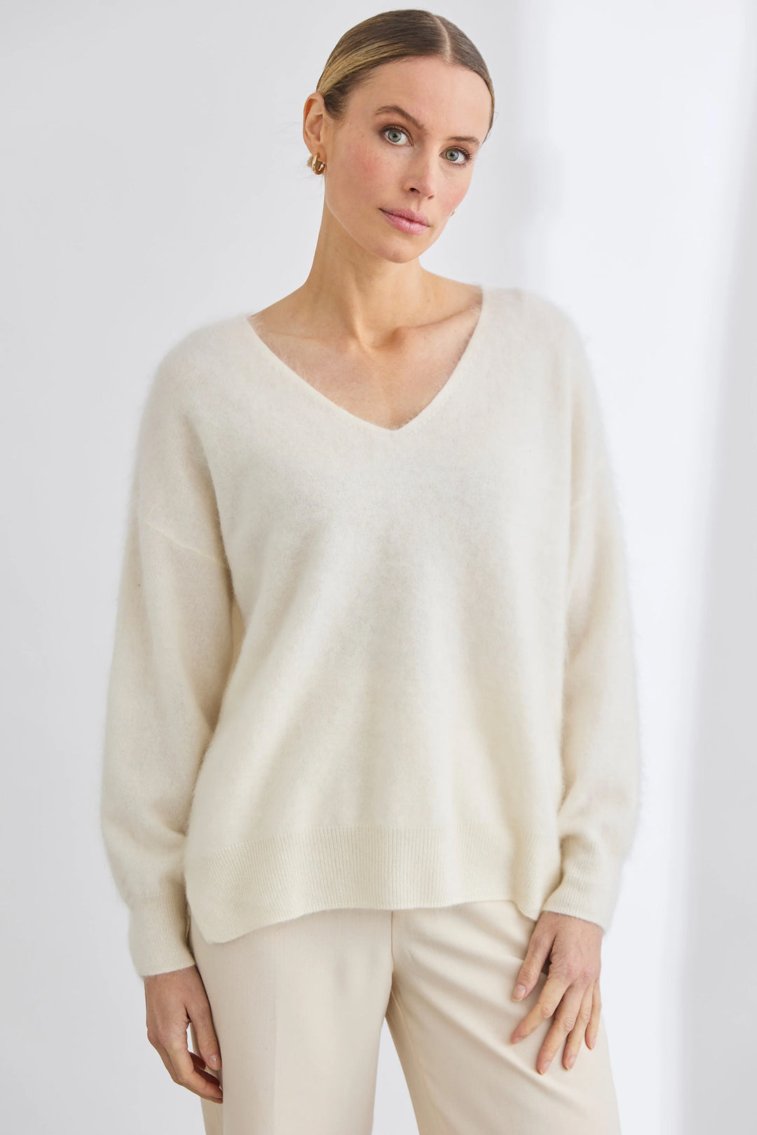 Woman wearing a beige sweater and pants against a white background