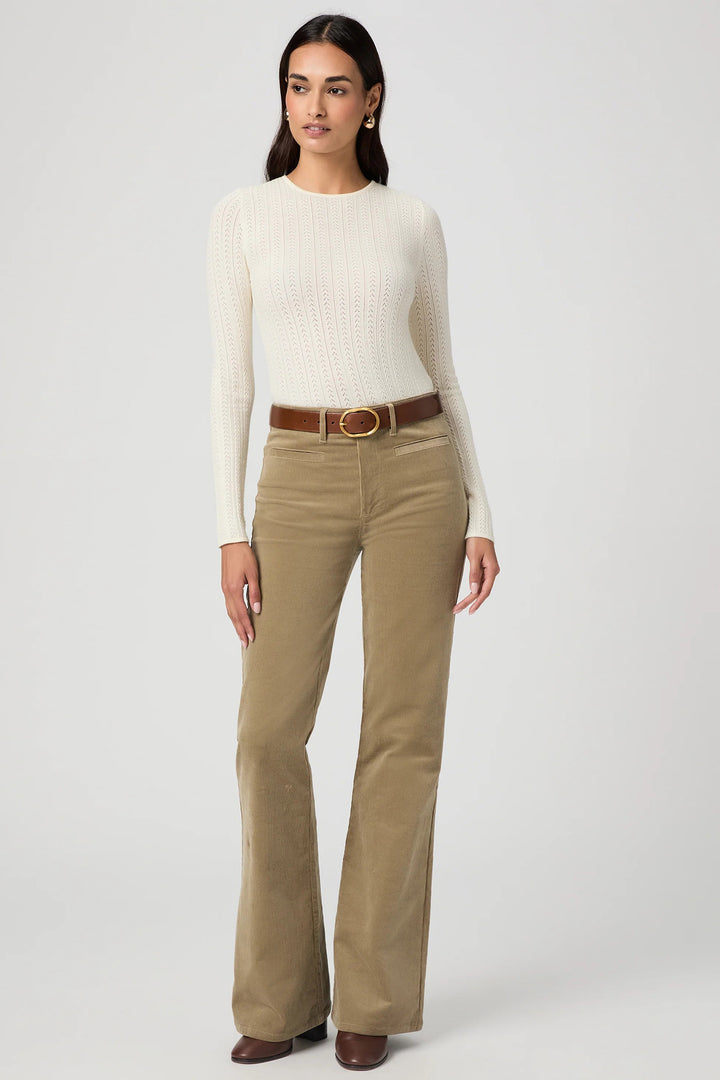 Woman wearing a white sweater and beige pants with a belt on a white background