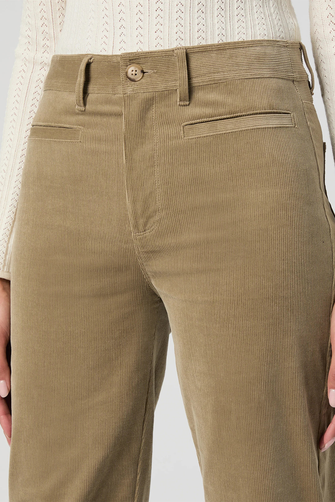 Close-up of brown corduroy pants with a white sweater background