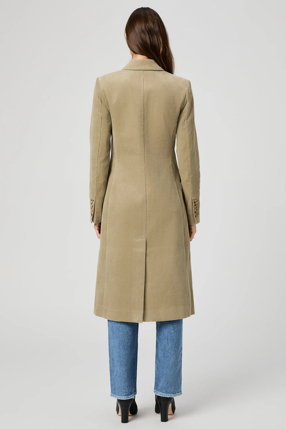 Person wearing a beige coat and blue jeans on a white background