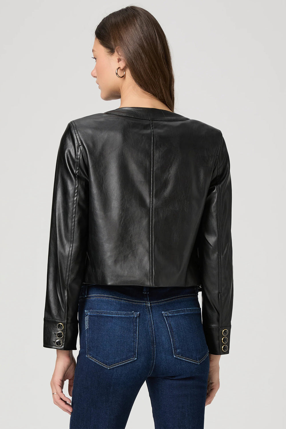 Person wearing a black leather jacket and blue jeans on a gray background