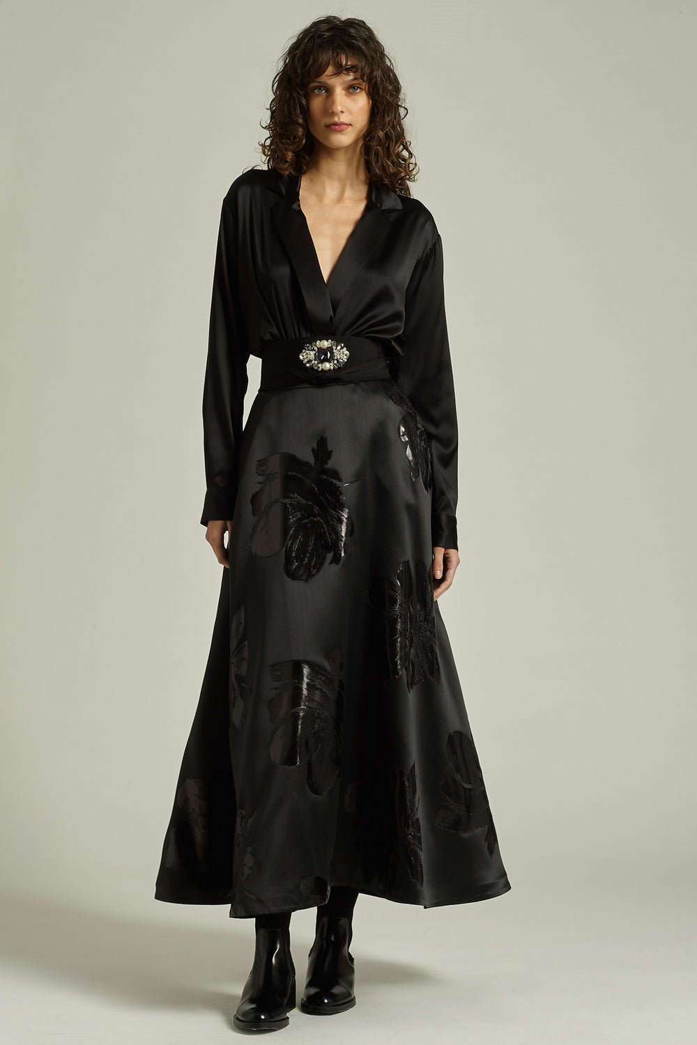 Woman wearing a black satin dress with a belt on a plain background