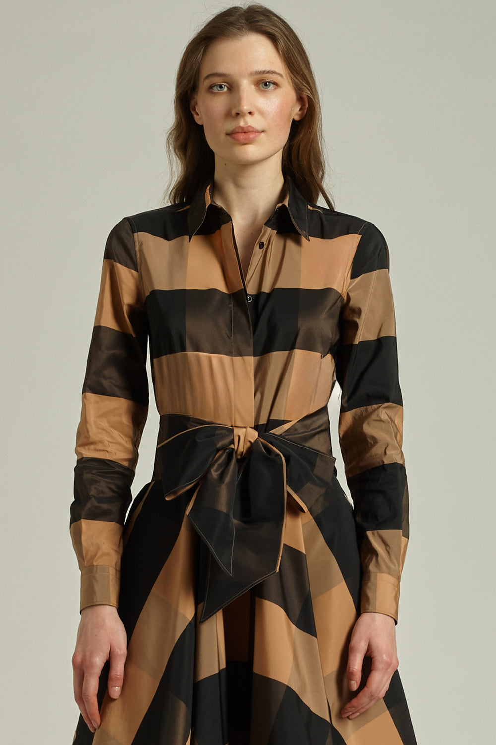 Woman wearing a long-sleeve, striped dress with a tie detail on a plain background