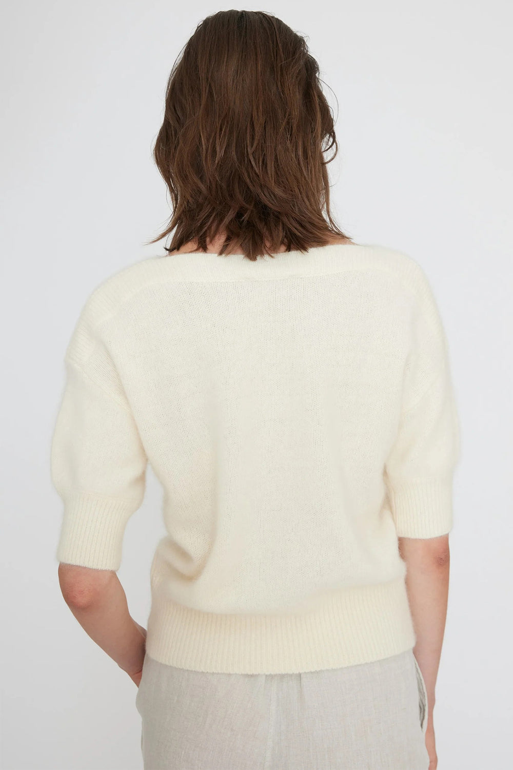 Person wearing a light-colored sweater on a plain background