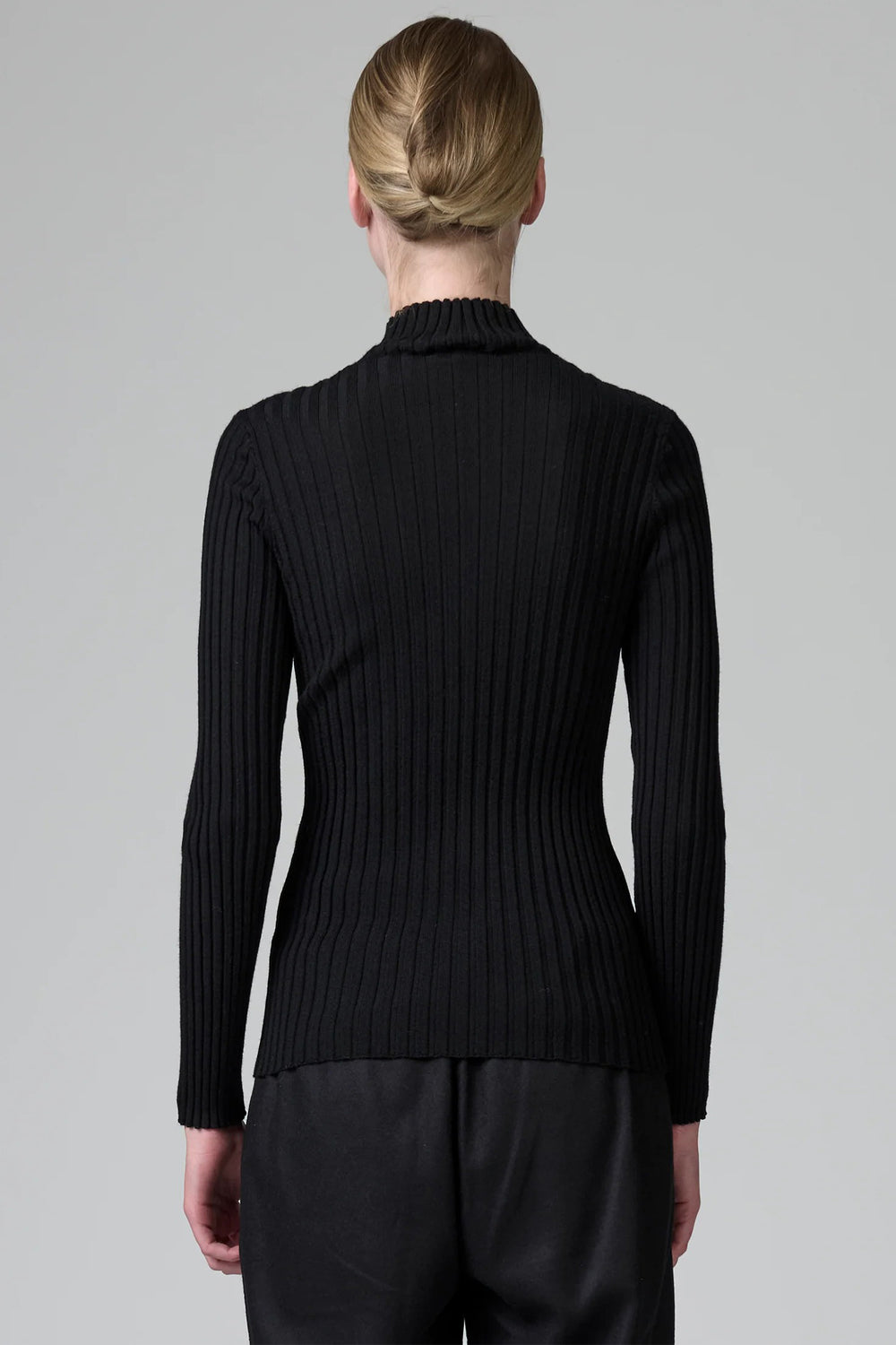 Person wearing a black ribbed sweater against a gray background