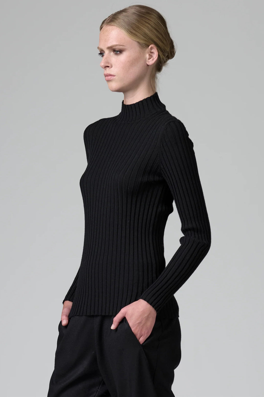 Woman wearing a black ribbed turtleneck sweater against a gray background