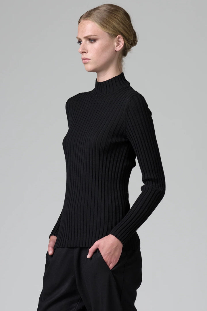 Woman wearing a black ribbed turtleneck sweater against a gray background