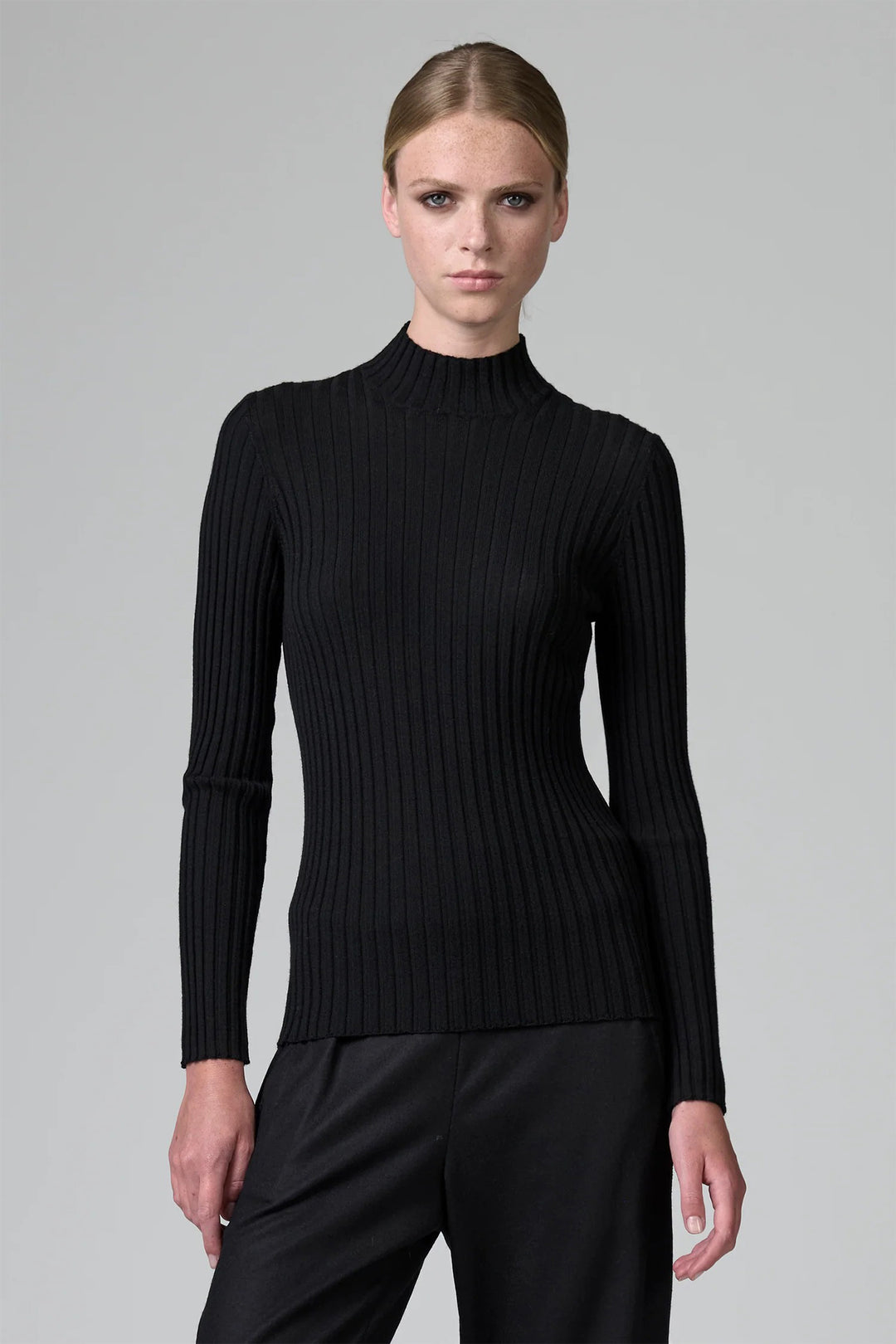 Woman wearing a black ribbed turtleneck sweater against a gray background
