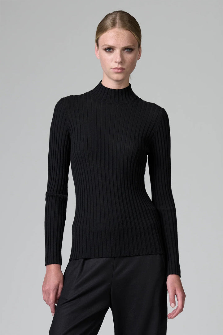 Woman wearing a black ribbed turtleneck sweater against a gray background