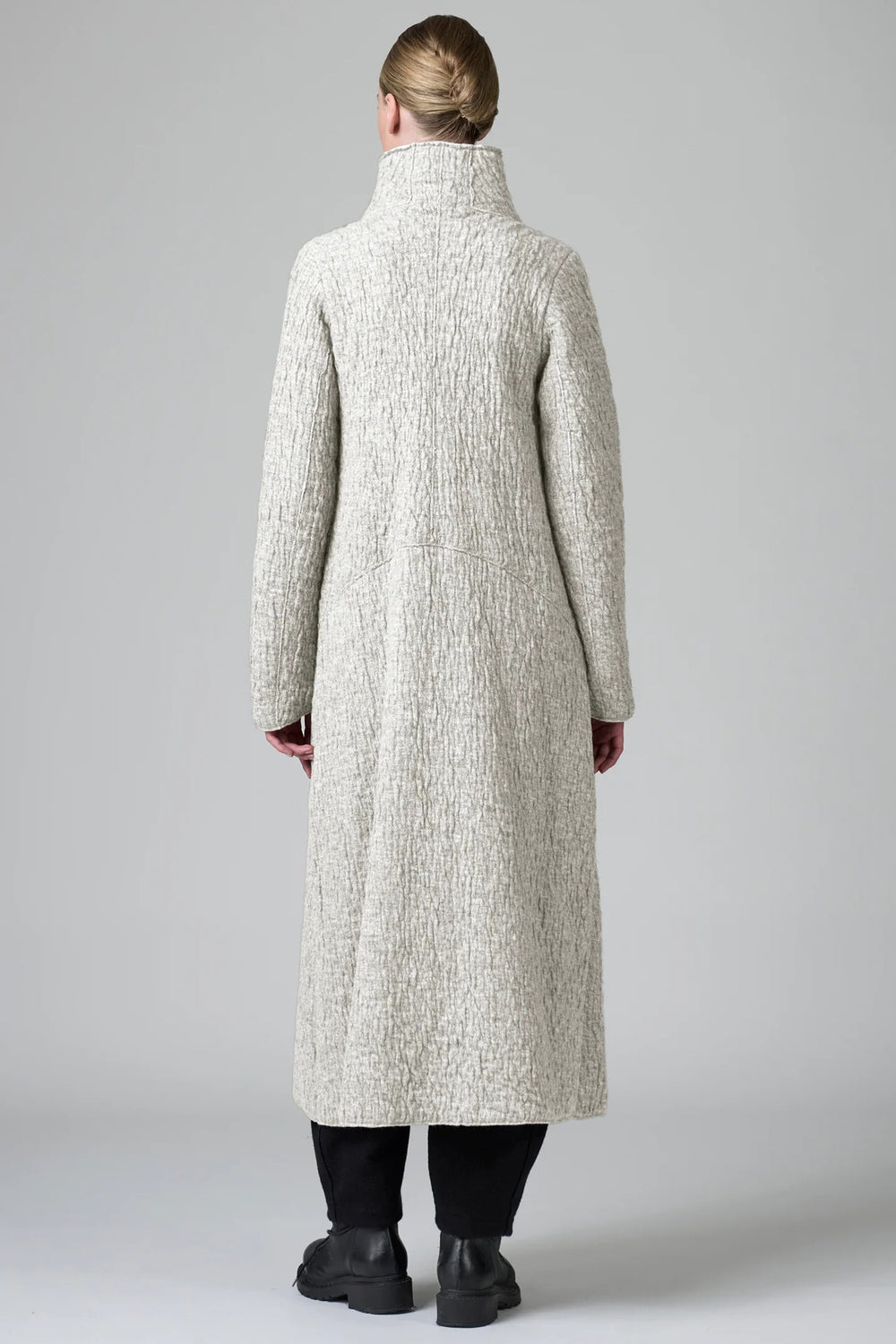 Person wearing a long textured coat from behind on a plain background